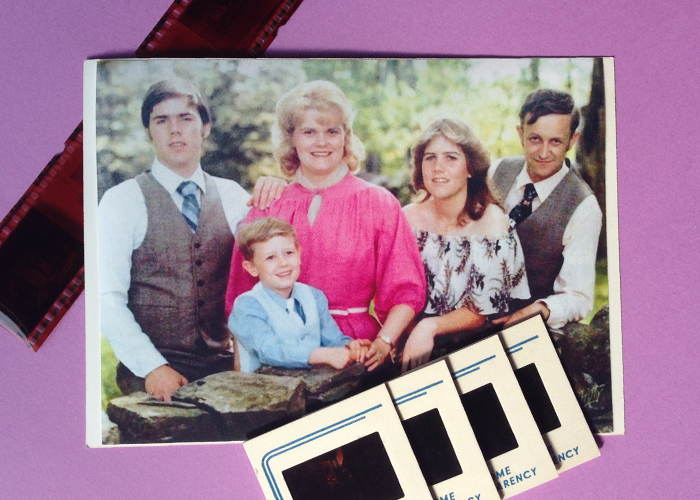 A family photo sits on a light purple background. On the left is a young man wearing a brown vest. To his left is is mother, with teased blonde hair and a hot pint chiffon dress on. In front of her is her youngest son, in a light blue collared shirt and matching vest. To mom's left is her daughter, wearing a patterned off the shoulder top. On the far end of the photo is Dad, also wearing a collared shirt and gray vest. He's staring right into the camera. Behind the top left corner of the photo sits a strip of film. Over the bottom right section of the image are 4 fanned out slides. 